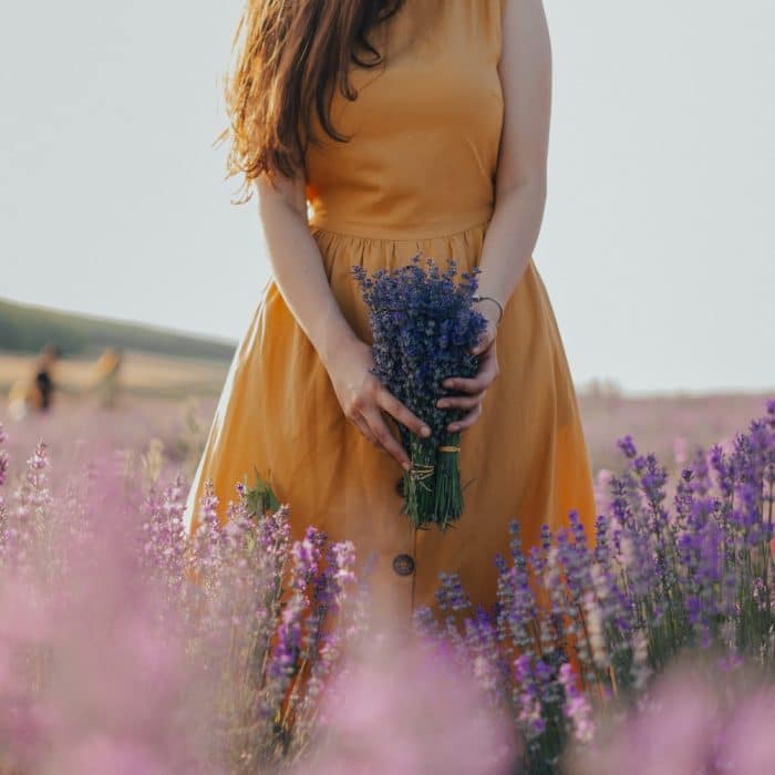 woman in yellow dress holding bouquet of lavender in a field of lavender